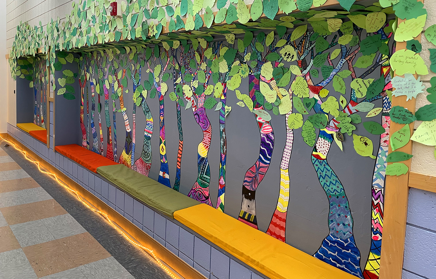 A wall covered with paper cutouts to make a forest. Leaves on the trees have statements of gratitude written on them.